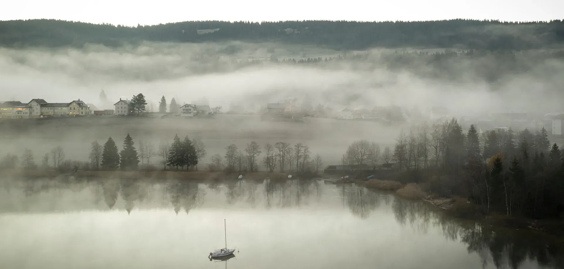 Brume matinale sur le lac, entre villages et forêts.